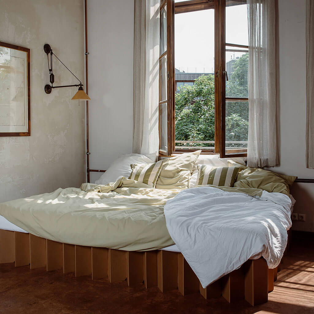 king size Bett 2.0, a top-quality cardboard bed frame by RIAB USA, with messy bedding and open window indicating morning