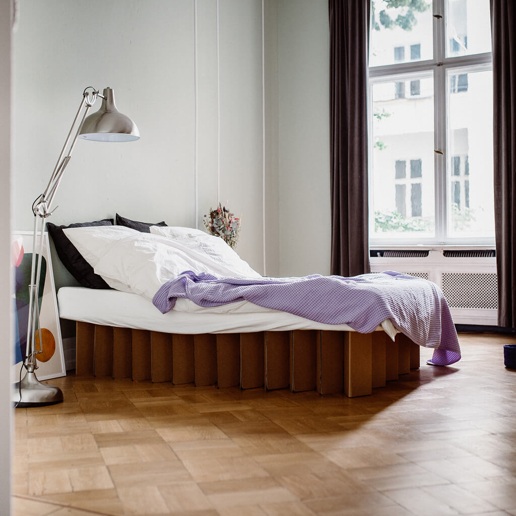 Bett 2.0, a sustainable cardboard bed frame by RIAB USA, surrounded by artwork, flowers, silver lamp in natural light