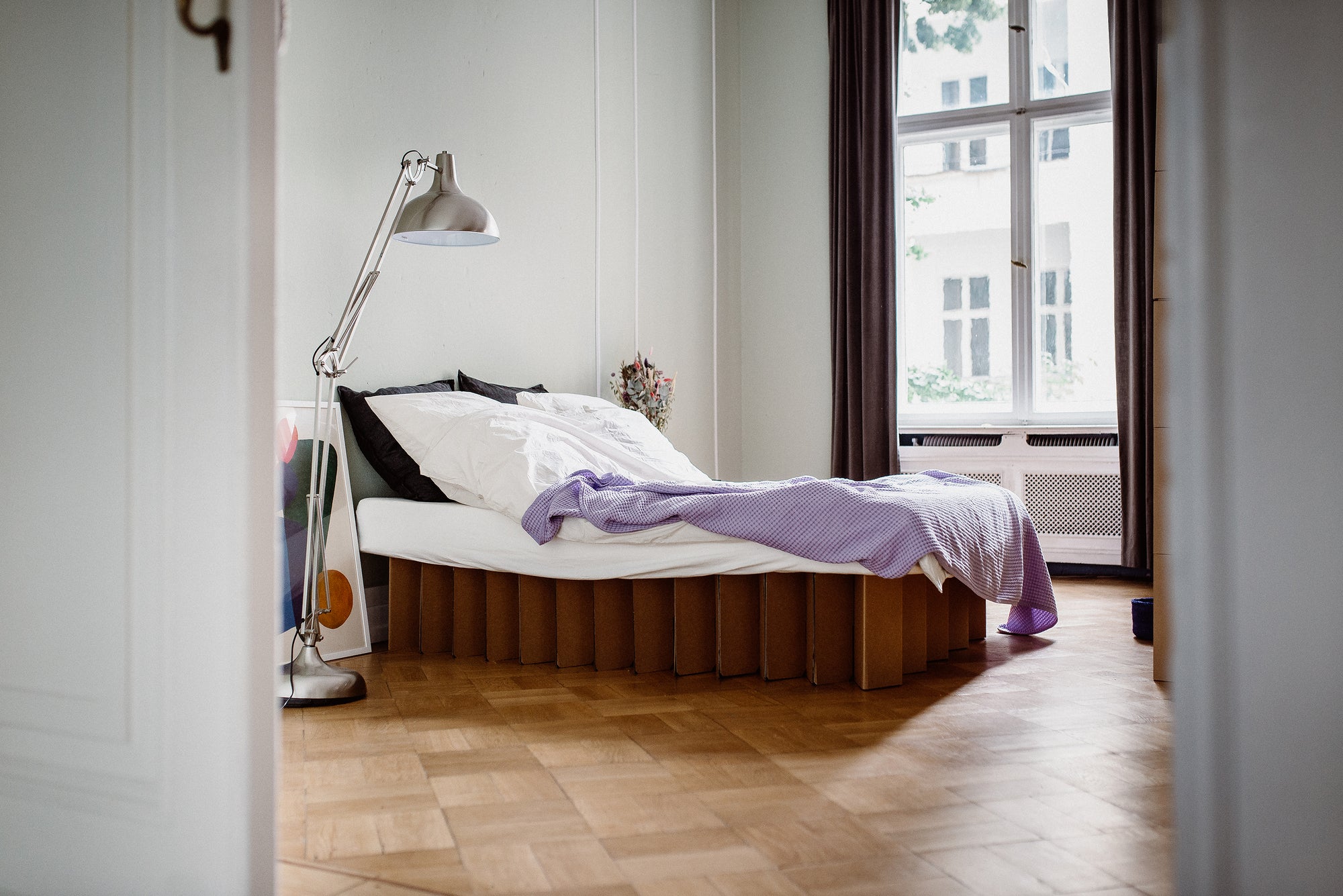 full size Bett 2.0, an eco-friendly bed frame by RIAB USA, on parquet floor with purple comforter and modern silver lamp